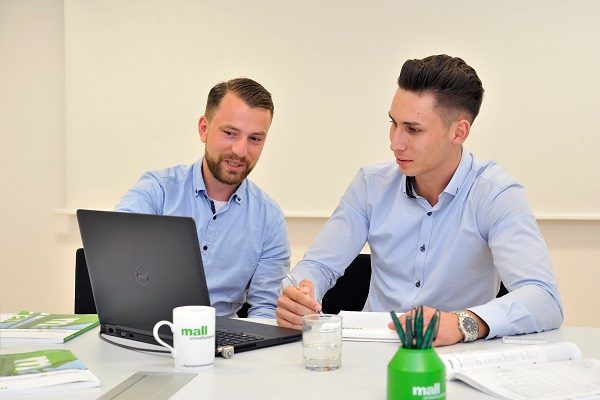 Zwei Männer sitzen am Schreibtisch und arbeiten am Computer.
